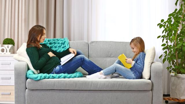 Pregnant mom and child sitting facing each other on a couch reading their books